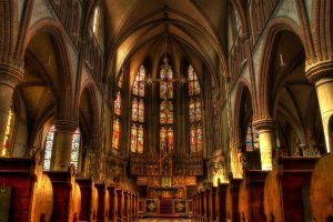 Innenbereich einer Kirche mit Altar, Bänken und hohen bunten Fernstern