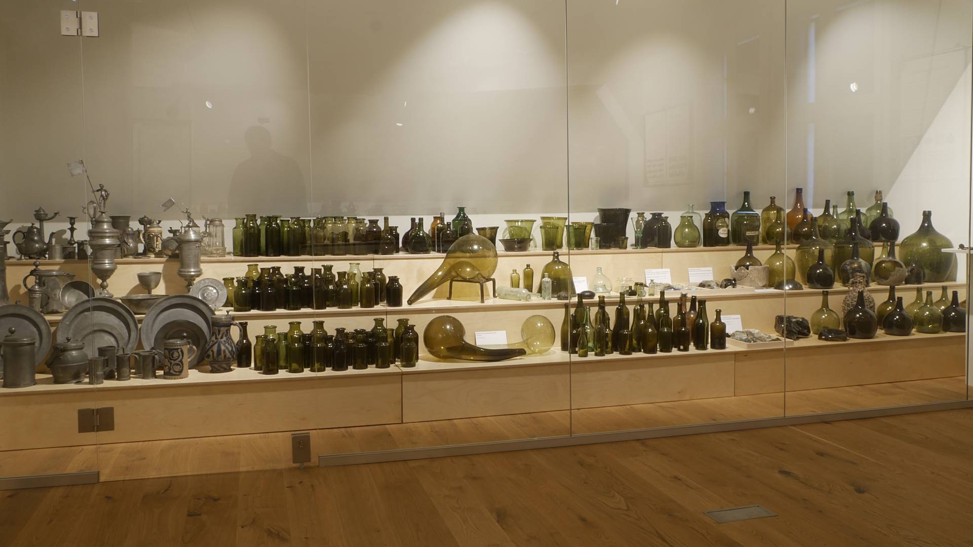 Gläser und weitere Ausstellungsobjekte aus Metall in verschiedenen Formen und Größen auf einem dreistufigem Regal